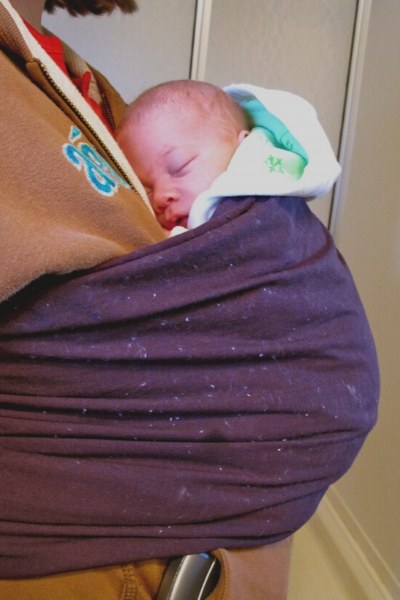newborn baby in a purple ring sling being worn by mother