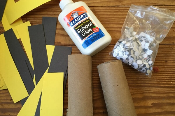 supplies for a bee craft: toilet paper tubes, yellow and black paper, googly eyes and glue