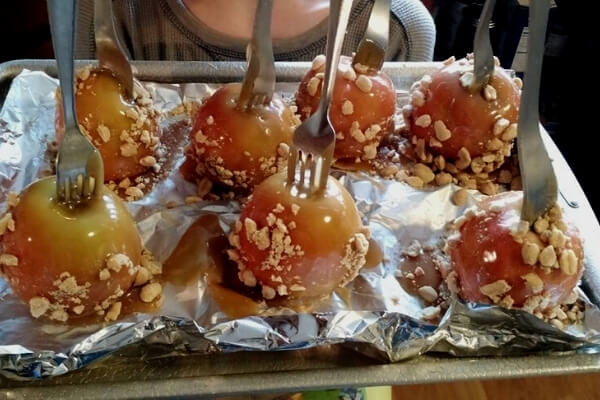 homemade caramel apples with nuts on top and forks for sticks