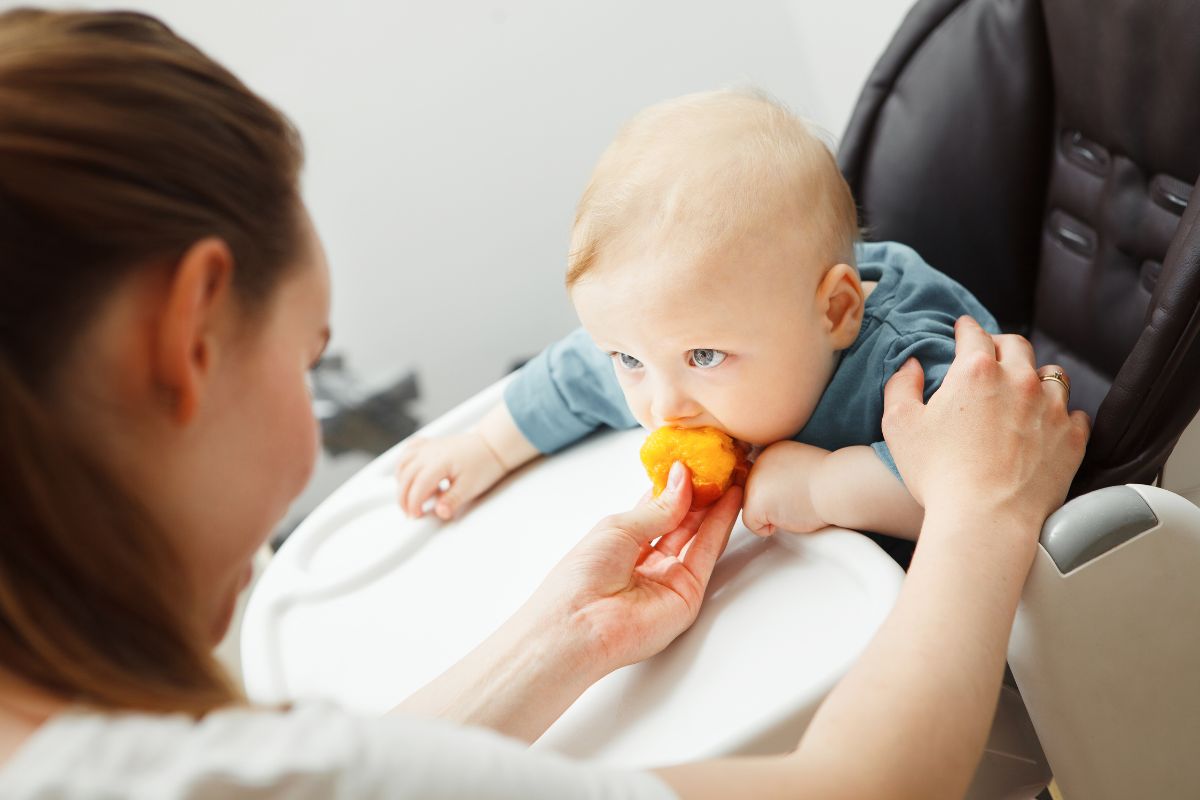 baby eating peach in high chair