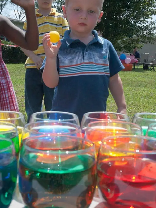 young boy tossing a ball into small jars of colored water