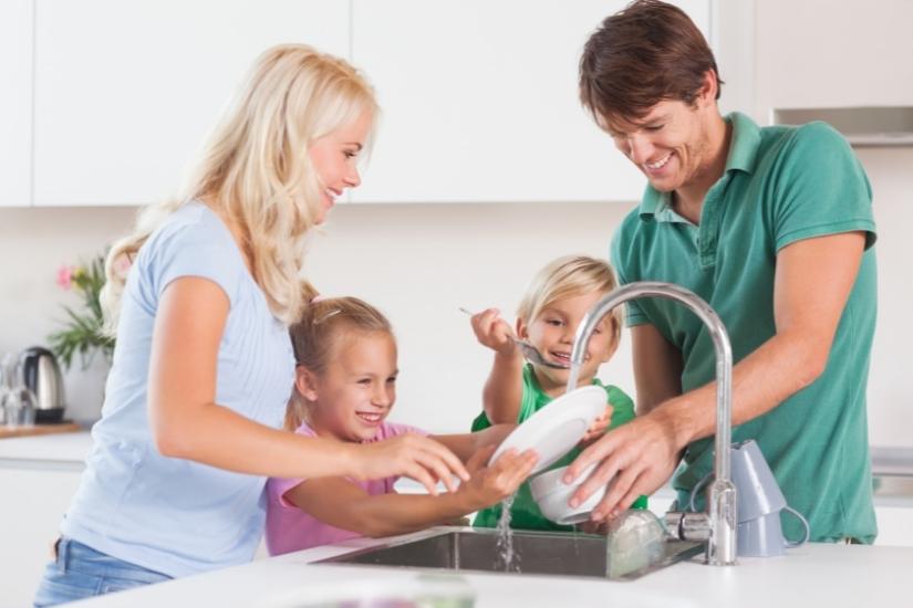 young family with 2 kids cleaning dishes together after a meal