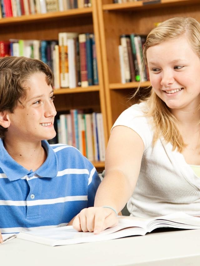 teen girl tutoring a younger boy in a library
