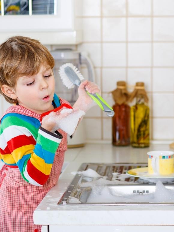 toddler boy washing dishes at a sink full of bubbles